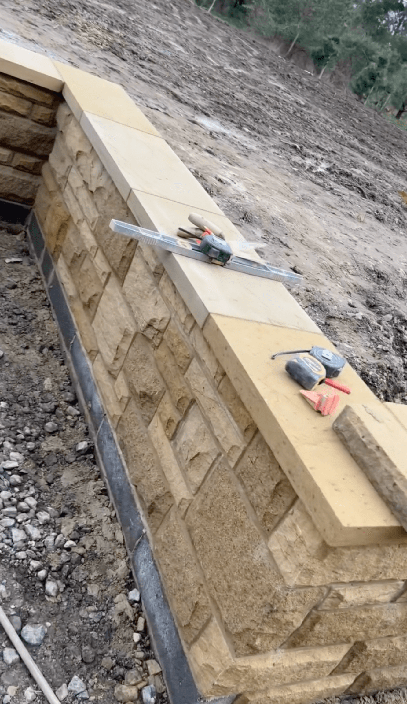 Stone garden wall under construction with masonry tools on the coping stones